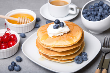 Pancakes with blueberries, cherries, sour cream, honey and coffee. Close-up. Selective focus.