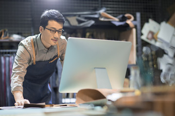 Young leather craftsman using computer in studio 