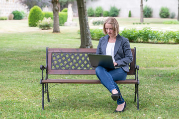 junge hübsche Frau sitzt im Park und schreibt am Laptop, virtual, Homeoffice, Videokonferenz, WLAN, 5G