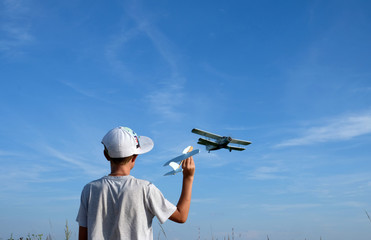Little boy with toy against sky with plane. Back view of kid in cap holding toy plane and standing...
