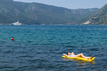 young adult woman on yellow mattress in blue sea water.