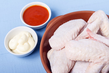 Chicken wings, mayonnaise and tomato sauce on a wooden table. Meat of poultry for cooking dietary...