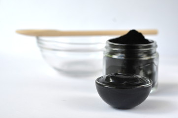 Cosmetic activated charcoal powder in a glass jar and beauty face mask mixture on white with copy space
