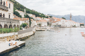 Fototapeta premium couple sitting at pier with beautiful view of sea and mountains
