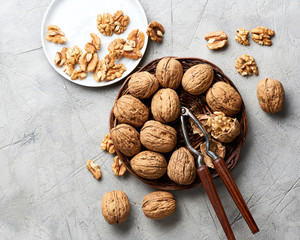 Whole walnuts and kernels on gray background and nutcracker.