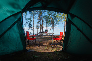 Camping in the middle of the forest, taken from inside the tent. View of the folding table and chairs with gas stove in the background of camping in the forest.