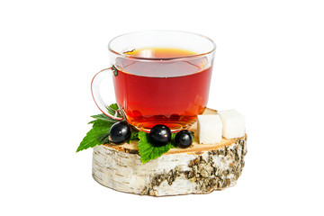 A glass mug of tea with berries of black currant and sugar cubes stands on a birch stump, isolated on a white background.