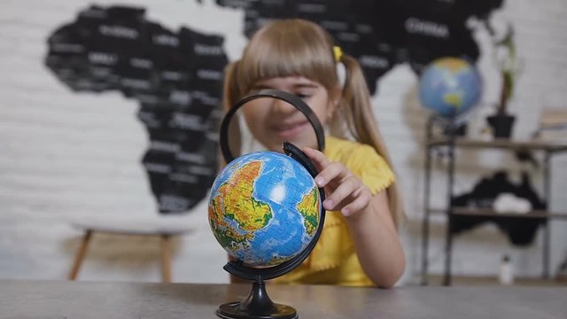 Portrait of a cute girl who playing looking in magnifying glass. Girl looking through a magnifying glass and studies the globe or map of the world