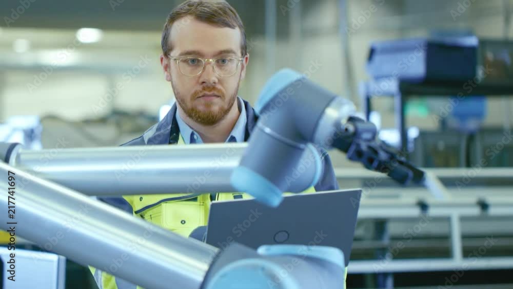 Poster At the Factory: Automation Engineer Uses Laptop for Programming Robotic Arm. New Era in Automatic Manufacturing Industry.