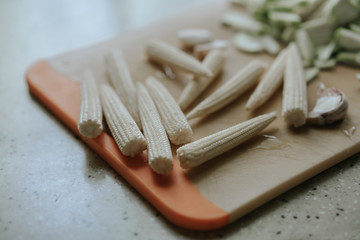 Young baby-corn, garlic and zucchini slices on an orange kitchen board