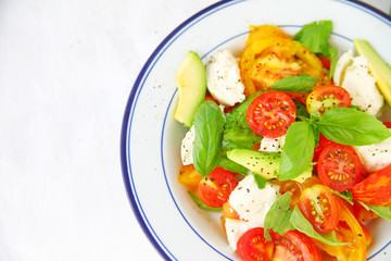 Overhead of fresh salad with cherry and heirloom tomatoes, avocado, burrata cheese, basil and black pepper