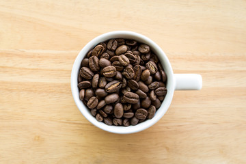 White coffee cup full of coffee beans on wooden background 