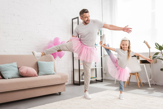 Front view of father and daughter in tutu skirts standing on one leg