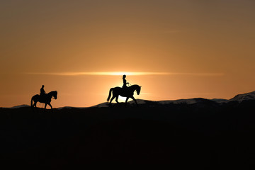 Obraz na płótnie Canvas Silhouette of man and woman riding horse across horizon as the sun goes down