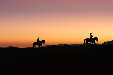 Fototapeta na wymiar Silhouette of man and woman riding horse across horizon as the sun goes down