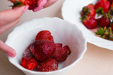 Woman cleans strawberries and puts it in a bowl. Close-up woman's hands.