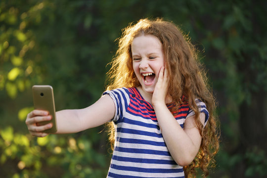 Little curly girl makes selfie photo outdoors.
