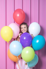 Fototapeta na wymiar Birthday girl with multicolored balloons against rose wall.