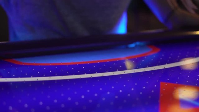 Slo-motion shot of a air hockey puck sliding past the player's hand into the goal. Then the player grabs the puck and places it back on the table and hits it.