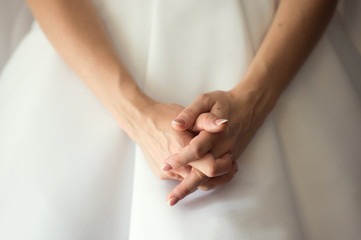 The crossed hands of bride in white wedding dress