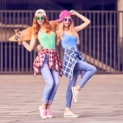 Two Young Woman Having Fun with Skateboard. Outdoor, Urban background. Playful Hipster Friend Enjoy Sunny day, Happy Smiling. Beautiful blond redhead Girl in Fashion Trendy Outfit.