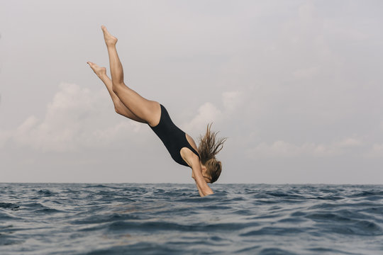 Side view of woman diving into sea against sky