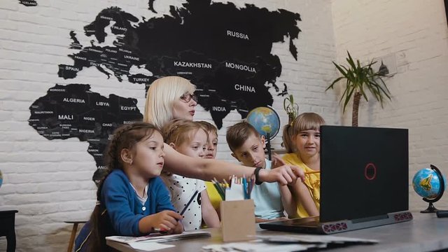 Young woman teacher discussing a computer program with a group of pupils. Female teacher using laptop with pupils in the classroom