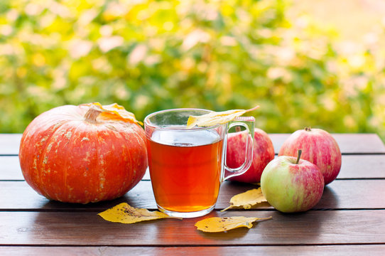 autumn background, pumpkin, apples with yellow leaves and tea in a cup on a wooden table in the garden.