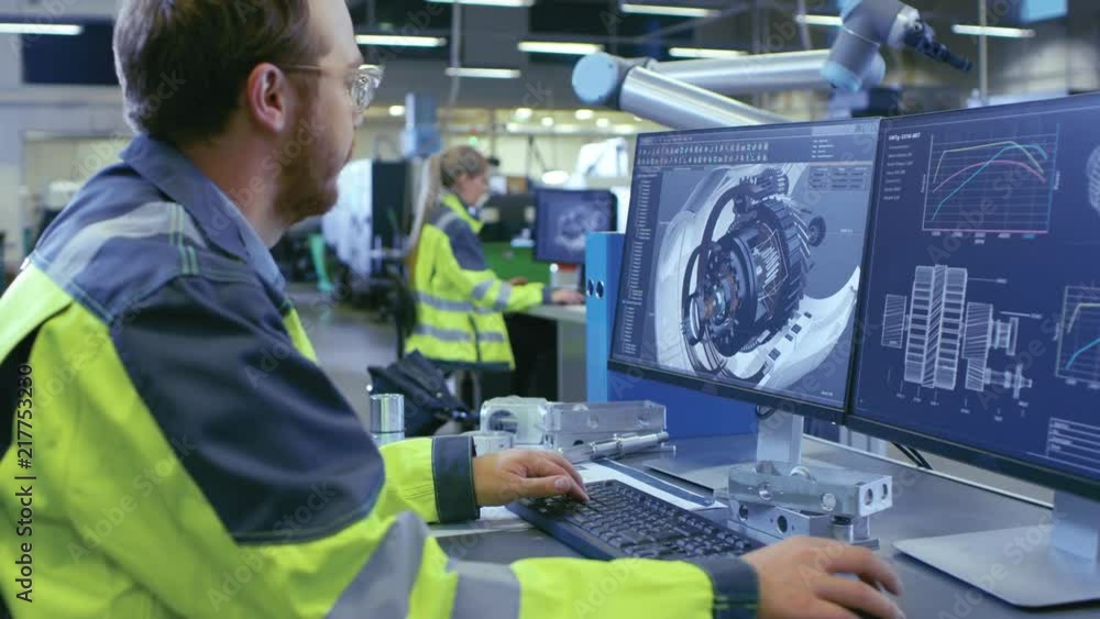 Poster At the Factory: Mechanical Engineer Works on Computer, Designs in CAD 3D Model of the Engine. In the Background Factory Workers and Functioning Robotic Arm. Shot on RED EPIC-W 8K Helium Cinema Camera.