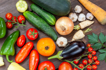 Colourful variety of fresh home grown vegetables from an organic garden on a wooden surface. Tomato, green and yellow bell peppers, carrot, parsley, onion, garlic, potato, eggplant and zucchini.