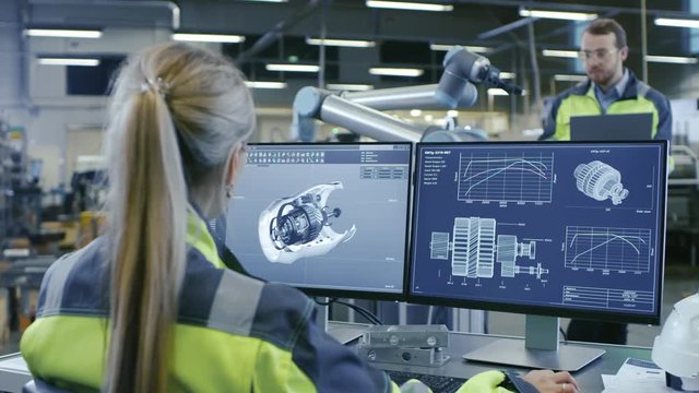 At the Factory:Female Mechanical Engineer Designs 3D Engine on Her Personal Computer Talks with Male Automation Engineer who Uses Laptop for Programming Robotic Arm