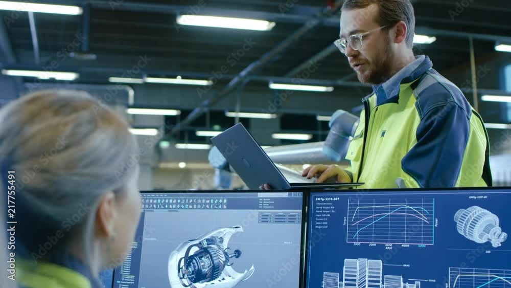Poster At the Factory: Male and Female Mechanical Engineers Use Laptop and Personal Computer while Discussing Robotic Arm Manufacturing Project. Screen Shows 3D Engine Concept made with CAD Software.