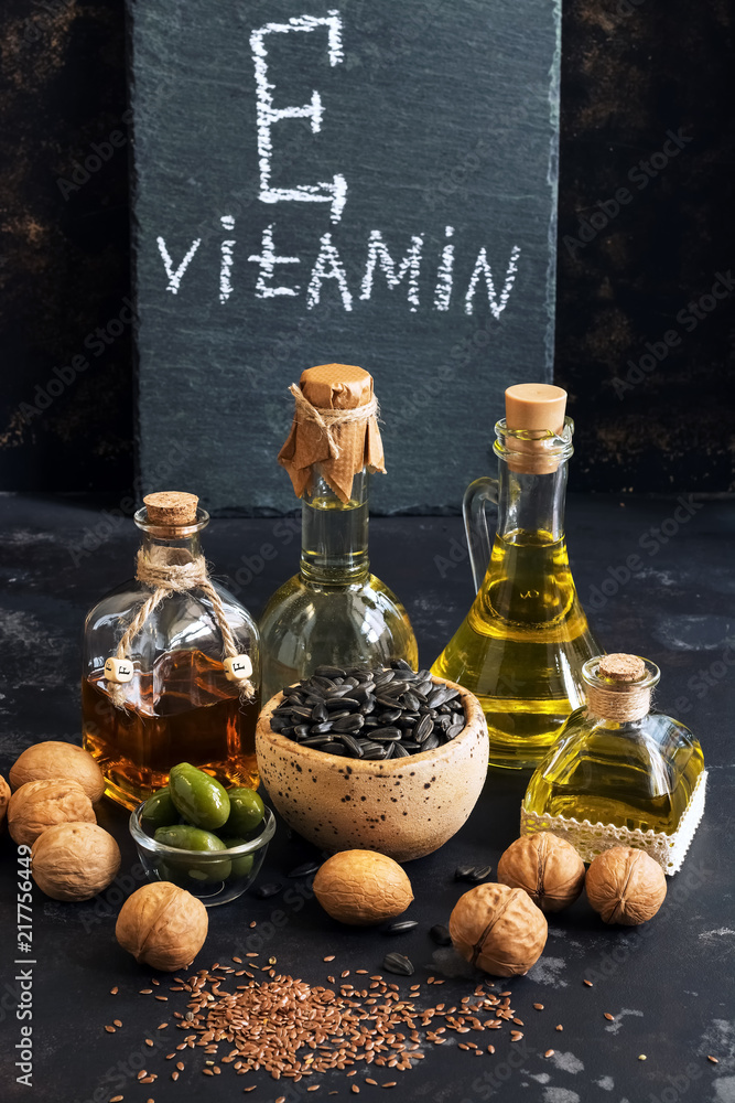 Wall mural Food rich in vitamin E on a black concrete background. Oil, seeds, nuts. Selective focus, sign with text. - Wall murals