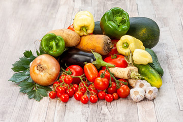 Colourful variety of fresh home grown vegetables from an organic garden on a wooden surface. Tomato, green and yellow bell peppers, carrot, parsley, onion, garlic, potato, eggplant and zucchini.