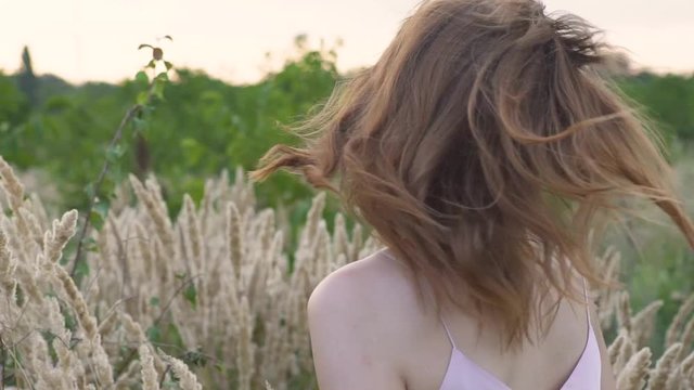 Close-up portrait of a young attractive red-haired woman in a field with spikelets. Slow motion
