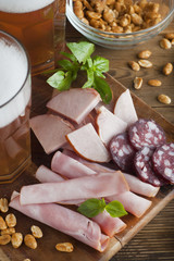 Variety of meat snacks to beer: ham, rolled meat, with fresh basil and glass beer over dark wooden background. Close up.