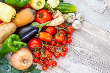 Colourful variety of fresh home grown vegetables from an organic garden on a wooden surface. Tomato, green and yellow bell peppers, carrot, parsley, onion, garlic, potato, eggplant and zucchini.