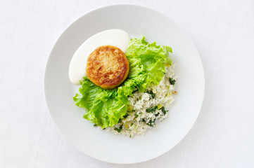 cabbage cutlet on lettuce leafs garnished with rice with leek, spinach, green onion, parsley, and dill served with mayo and sour cream sauce