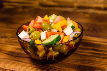 Glass bowl with greek salad on wooden table