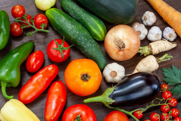 Colourful variety of fresh home grown vegetables from an organic garden on a wooden surface. Tomato, green and yellow bell peppers, carrot, parsley, onion, garlic, potato, eggplant and zucchini.