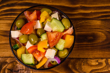 Glass bowl with greek salad on wooden table. Top view
