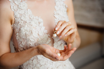 Close-up of a cropped frame of a girl in a white lace dress with embroidery holding in hands a pearl earring. The bride is going to the wedding.
