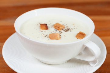 White cup of mushroom soup with crispy bread on wood table, appetizer before main dishes.
