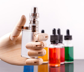 Mannequin hand holding electronic cigarette. Bottles with vape liquid on background