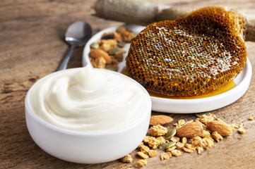 Healthy flavored yogurt in ceramic bowl with granola and honeycomb on the wooden background with copy space for your text.