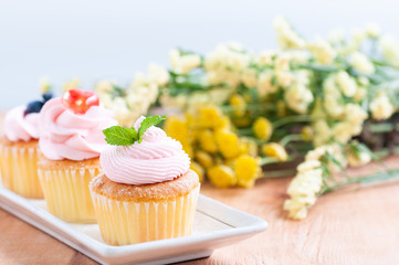 Group of cupcakes arrange on long white plate on table with blur flowers background, dessert bakery in minimal concept.  Bakery advertise in menu.