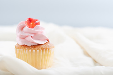 Single butter cup cake with strawberry cream and red cherry on table and soft cloth with blur background, bakery dessert for party.
