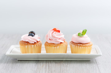 Group of cupcakes arrange on long white plate on table with blur background, dessert bakery in minimal concept.  Bakery advertise in menu.