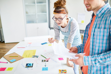 Obraz premium One of students looking at picture while leaning over table and discussing ideas for project with groupmate