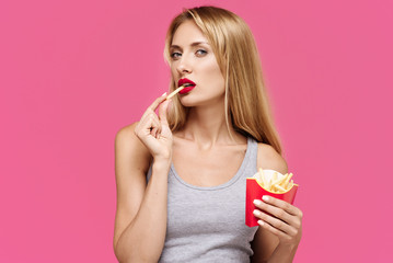 Young beautiful slender girl with a pink background eating a french fries. Concept of un healthy...